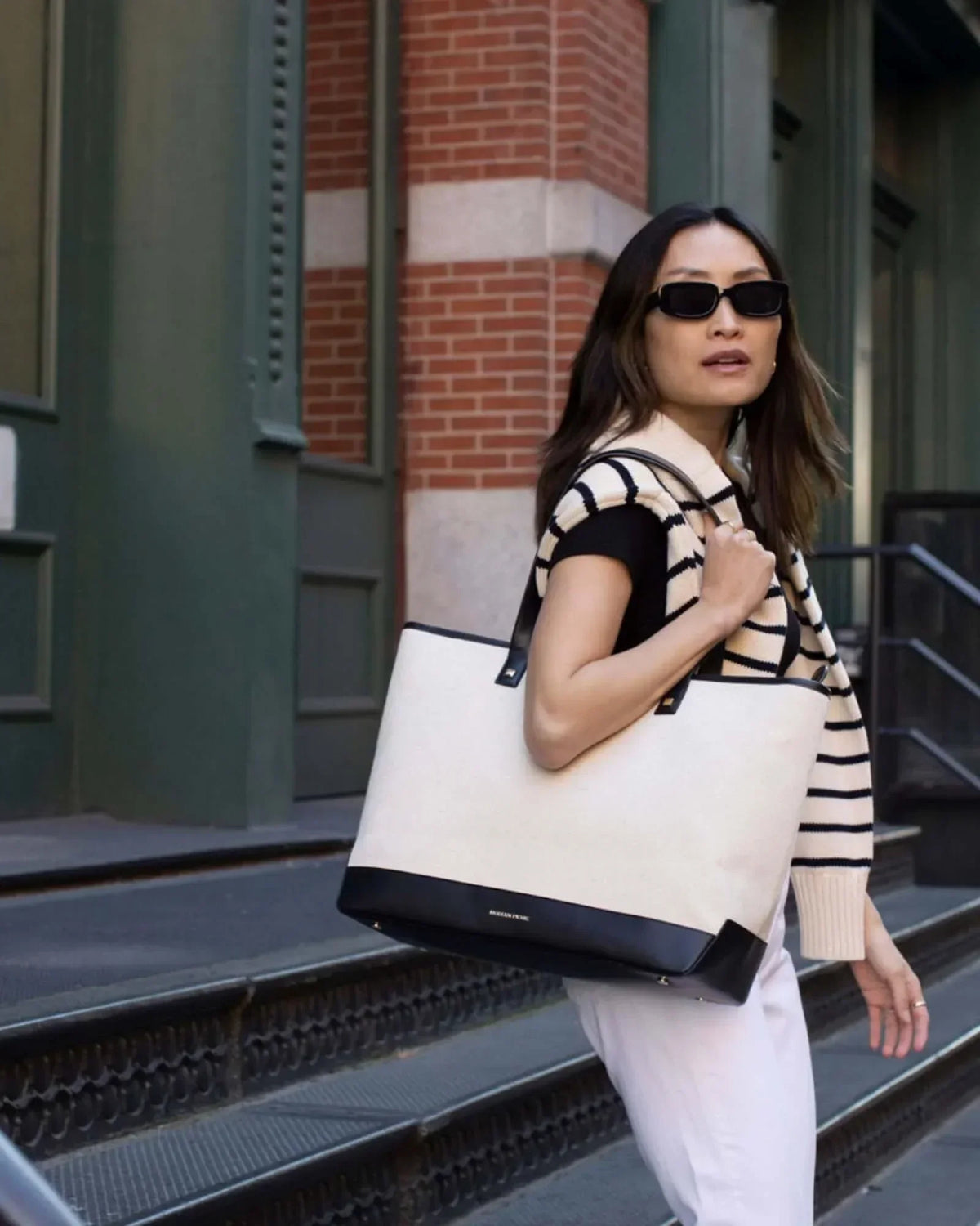 Stylish woman carrying chic cream and black tote bag on city steps, perfect for work or travel