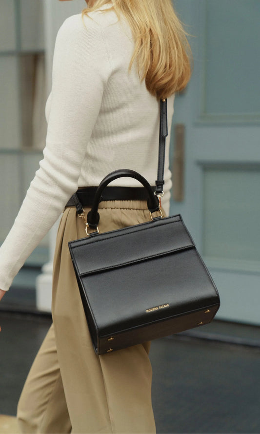 Black vegan leather lunch tote with top handle and shoulder strap, styled for work or travel.