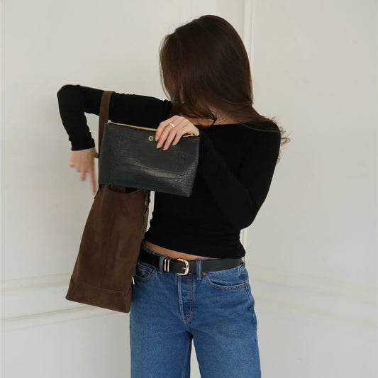 Woman placing black vegan leather insulated lunch bag into brown tote, stylish casual outfit