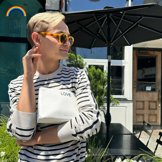 Person in striped shirt holding white insulated lunch bag with rainbow 'LOVE' text outdoors