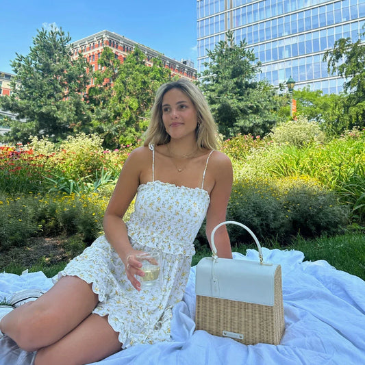 Woman picnicking on grass with chic insulated lunch bag and glass of water