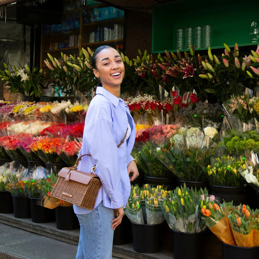 Woman with a stylish brown lunch bag in front of a flower shop, surrounded by bouquets.