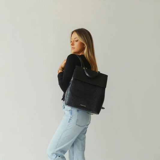 Woman wearing a black vegan leather insulated backpack with gold hardware
