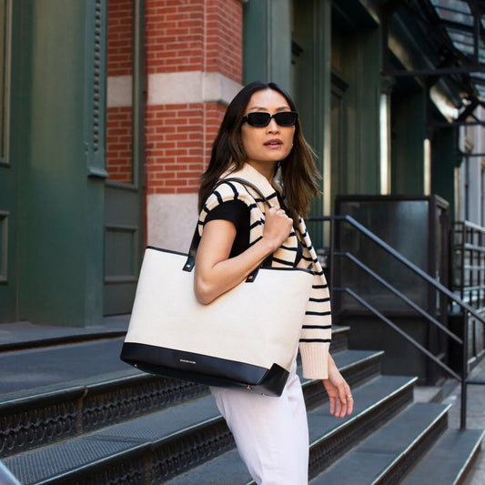 Woman in sunglasses carrying a large insulated tote bag on city steps, striped sweater draped over shoulders