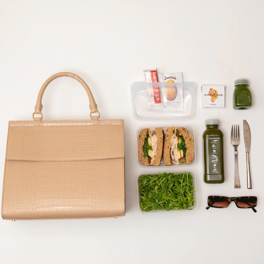 Beige vegan leather lunch bag with salad, sandwich, snacks, green juice, sunglasses, and utensils