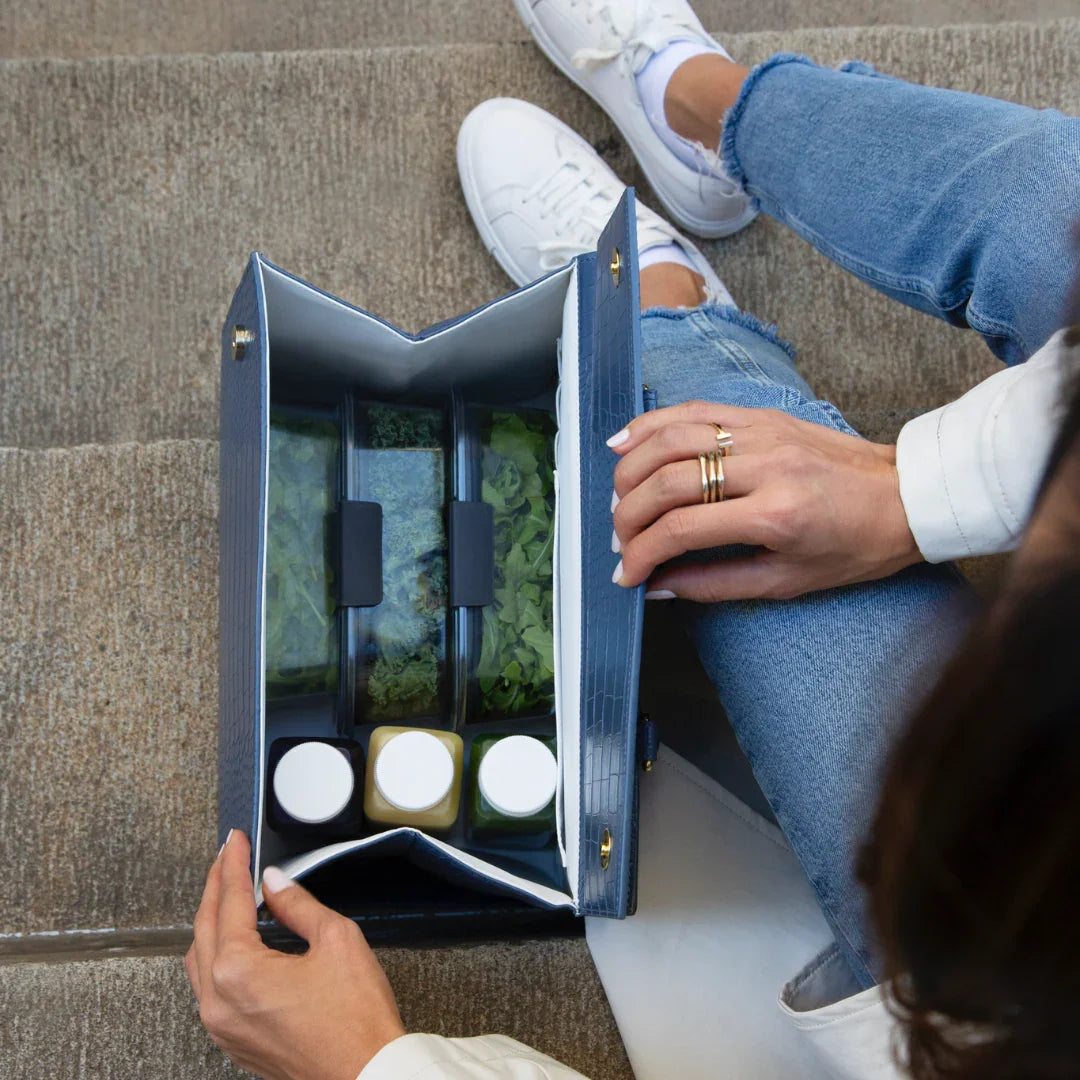 Woman holding navy insulated lunch bag with salad containers and juice bottles on outdoor steps
