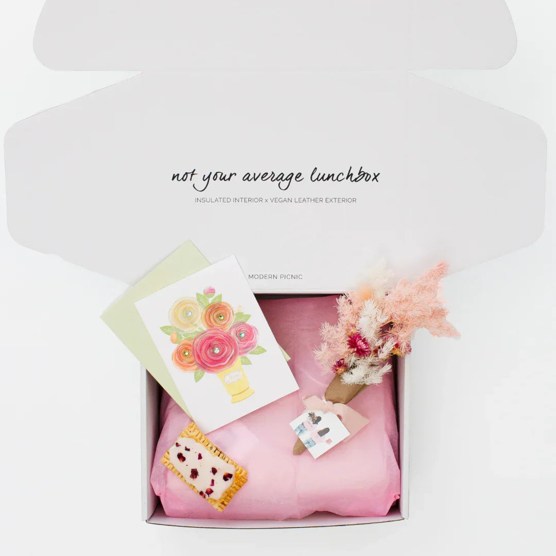 Gift box with vegan leather lunch bag, floral card, dried bouquet, and pastry on pink tissue