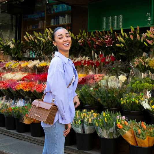 Woman with woven vegan leather lunch bag by a flower shop, surrounded by colorful bouquets.