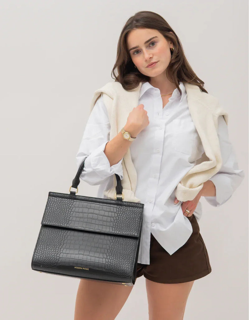 Woman holding black croc-texture vegan leather tote bag, styled for work or travel with white shirt and cardigan