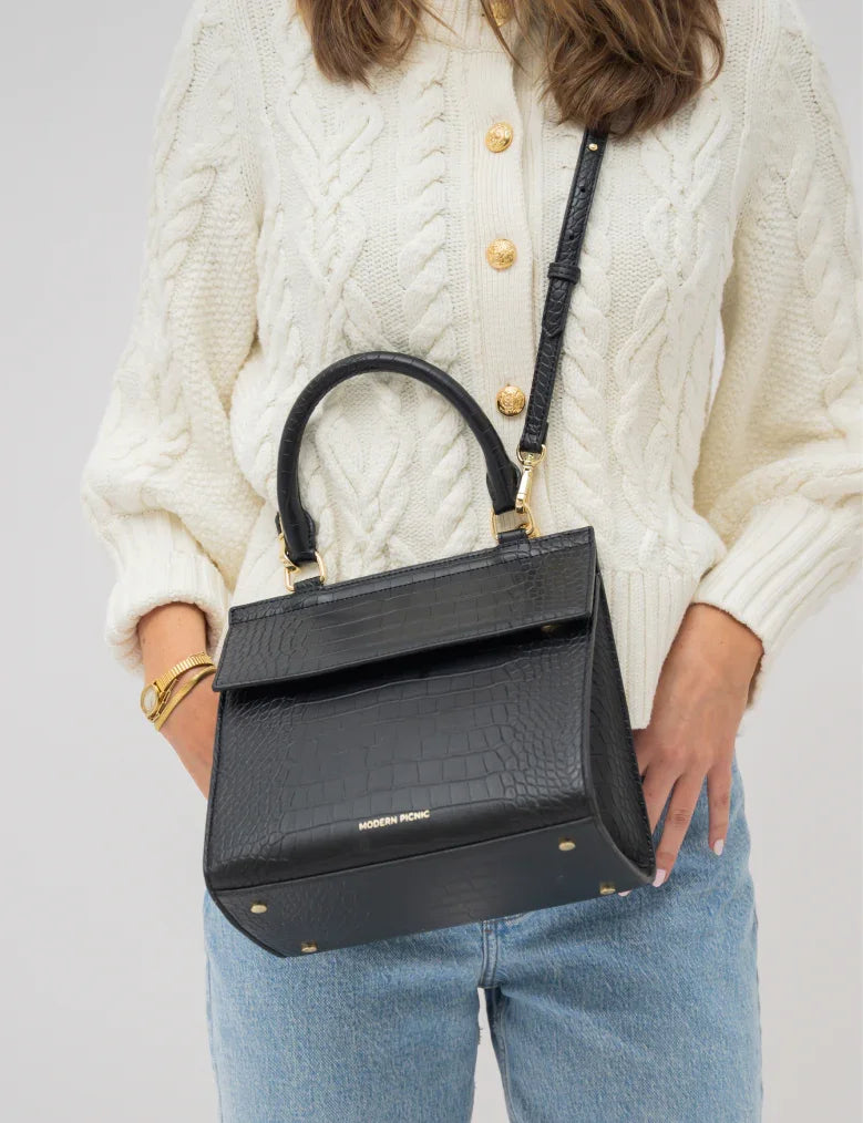 Black croc-texture vegan leather handbag with gold hardware, styled with cream sweater and jeans