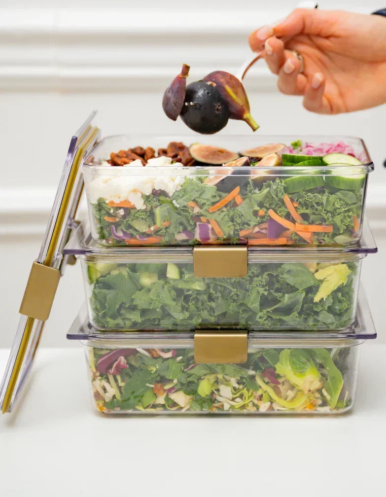 Stacked clear meal prep containers with fresh salads, figs, and veggies for healthy lunches