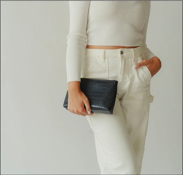Woman holding black croc-texture vegan leather clutch, styled with white top and pants for chic everyday look