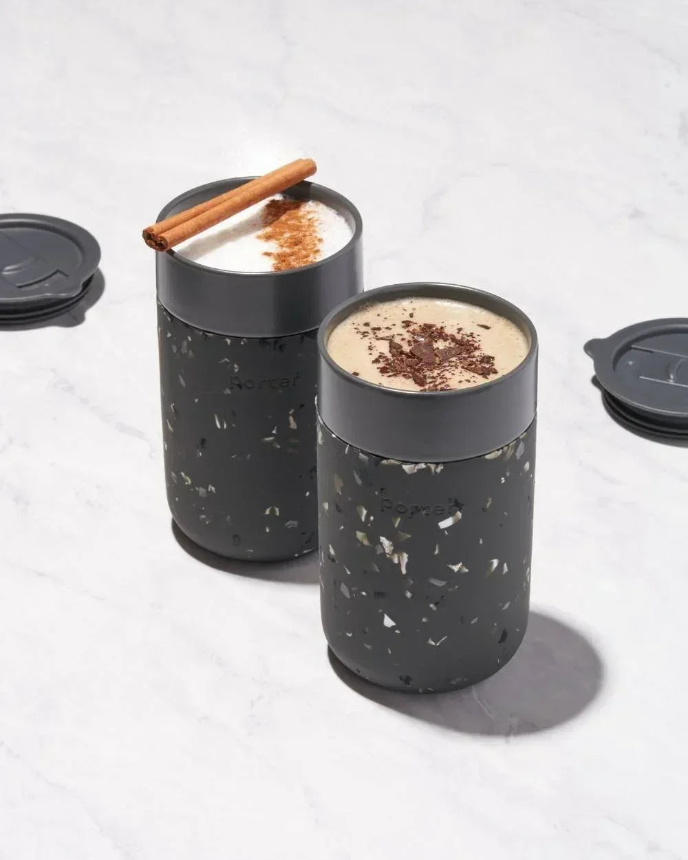 Speckled gray travel mugs with cinnamon stick and chocolate shavings, perfect for on-the-go coffee or tea.