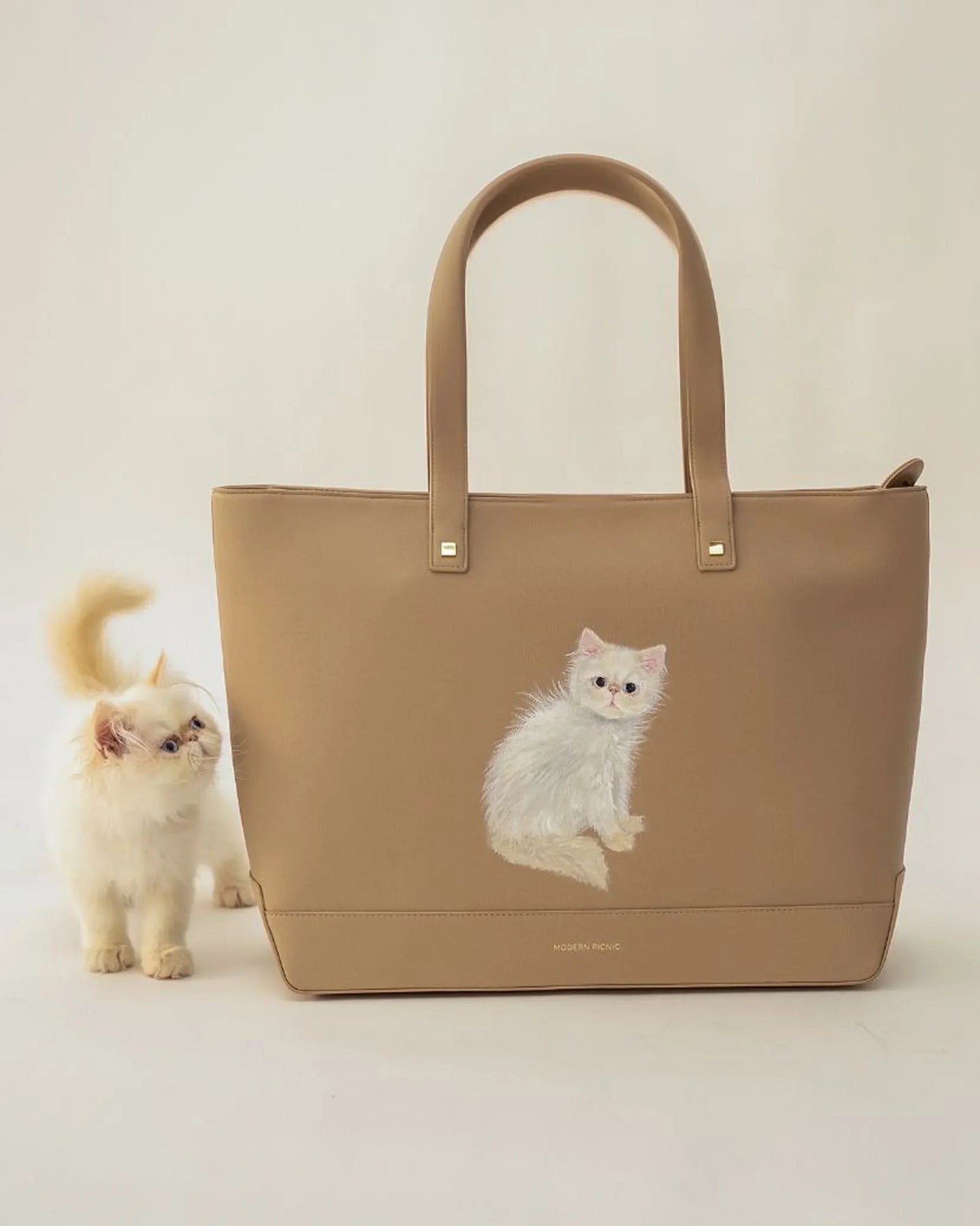 Beige vegan leather tote bag with cute cat print, styled with fluffy white kitten beside it