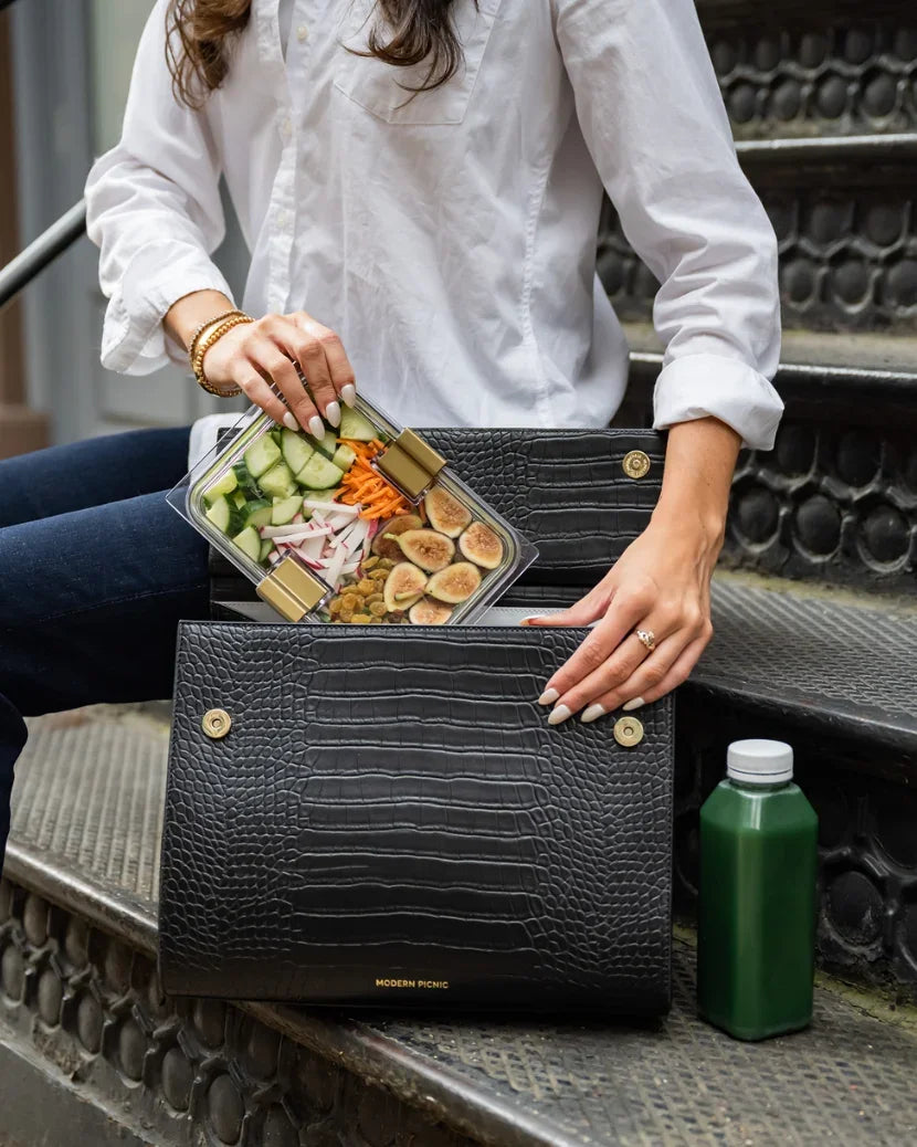 Person putting a healthy meal container into a black vegan leather Modern Picnic lunch bag.