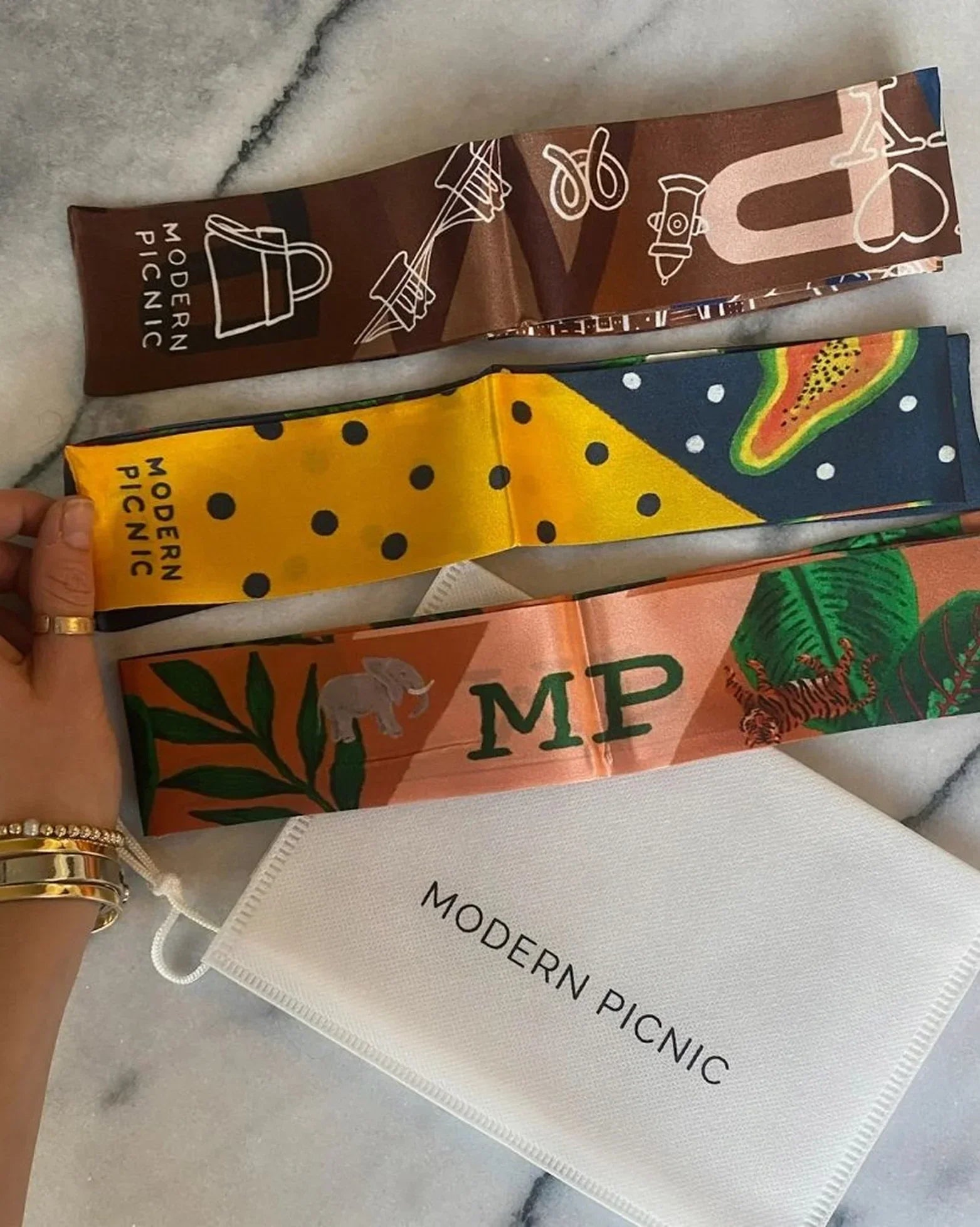 Colorful Modern Picnic scarves with playful designs and branding on marble surface