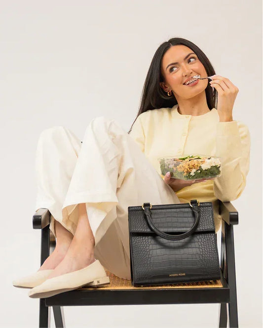 Woman enjoying salad with stylish black vegan leather tote beside her, perfect for work or travel.