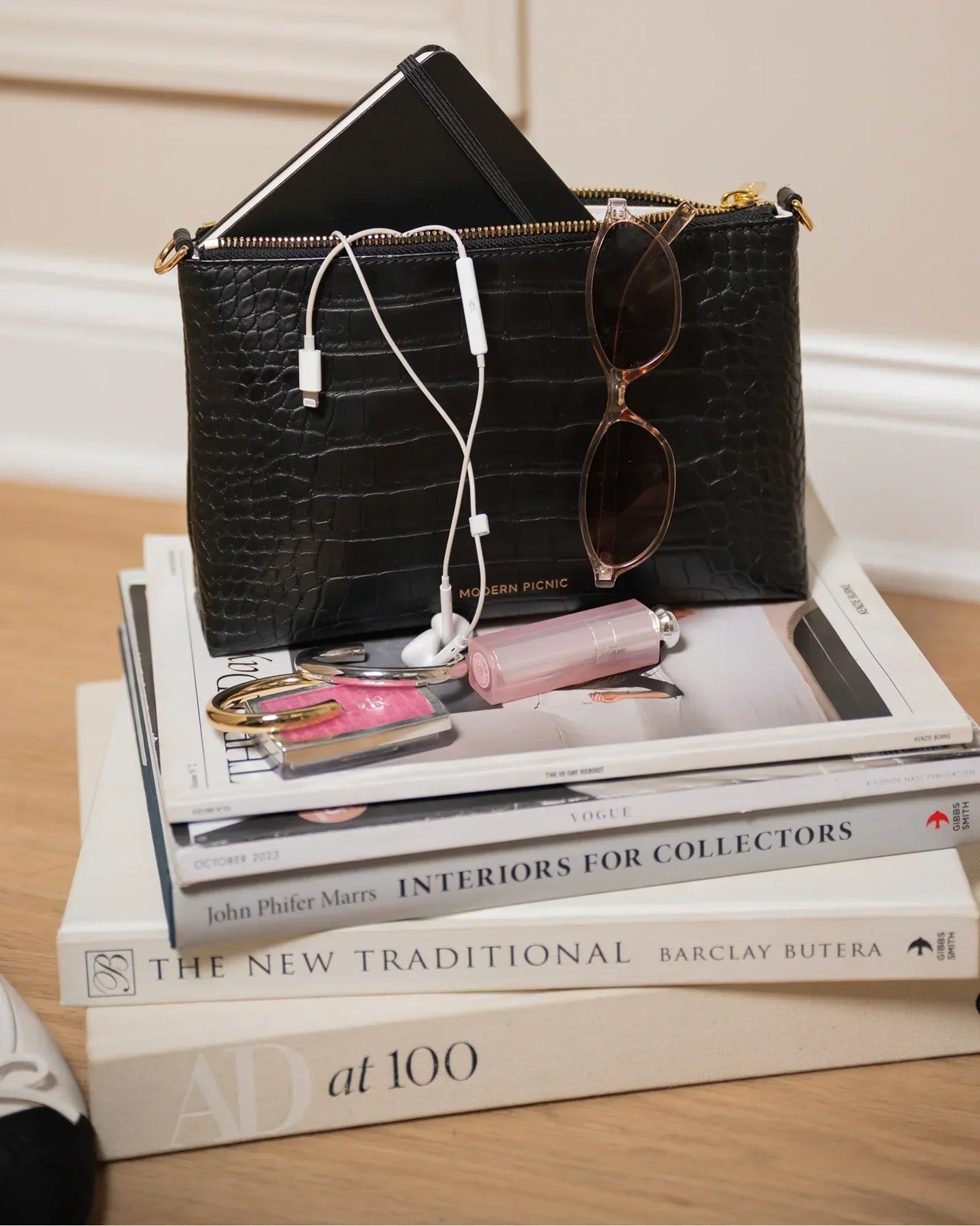 Black textured pouch with earphones, sunglasses, and lipstick on stacked books