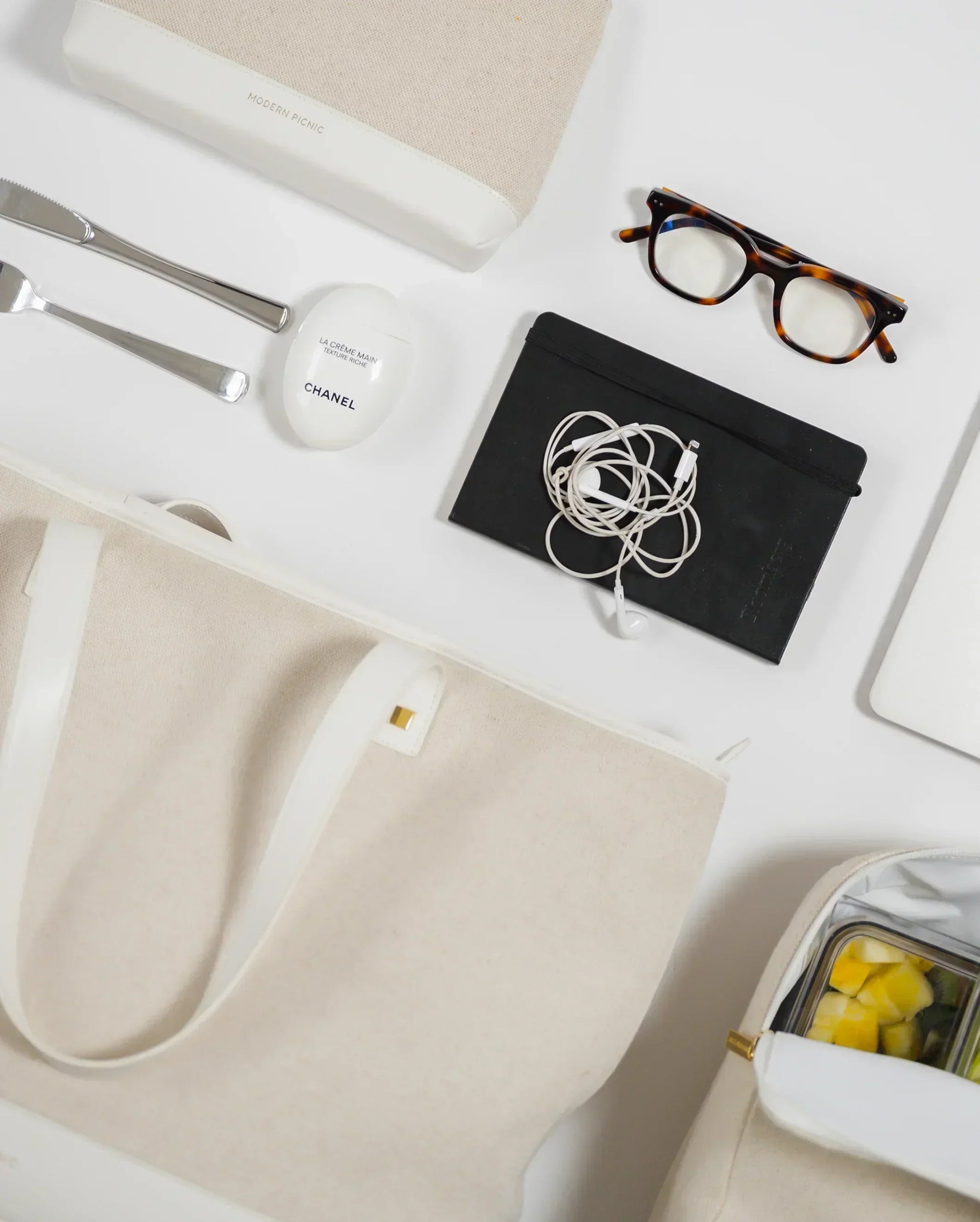 Stylish beige tote with insulated lunch bag, earphones, glasses, and Chanel hand cream for modern professionals.