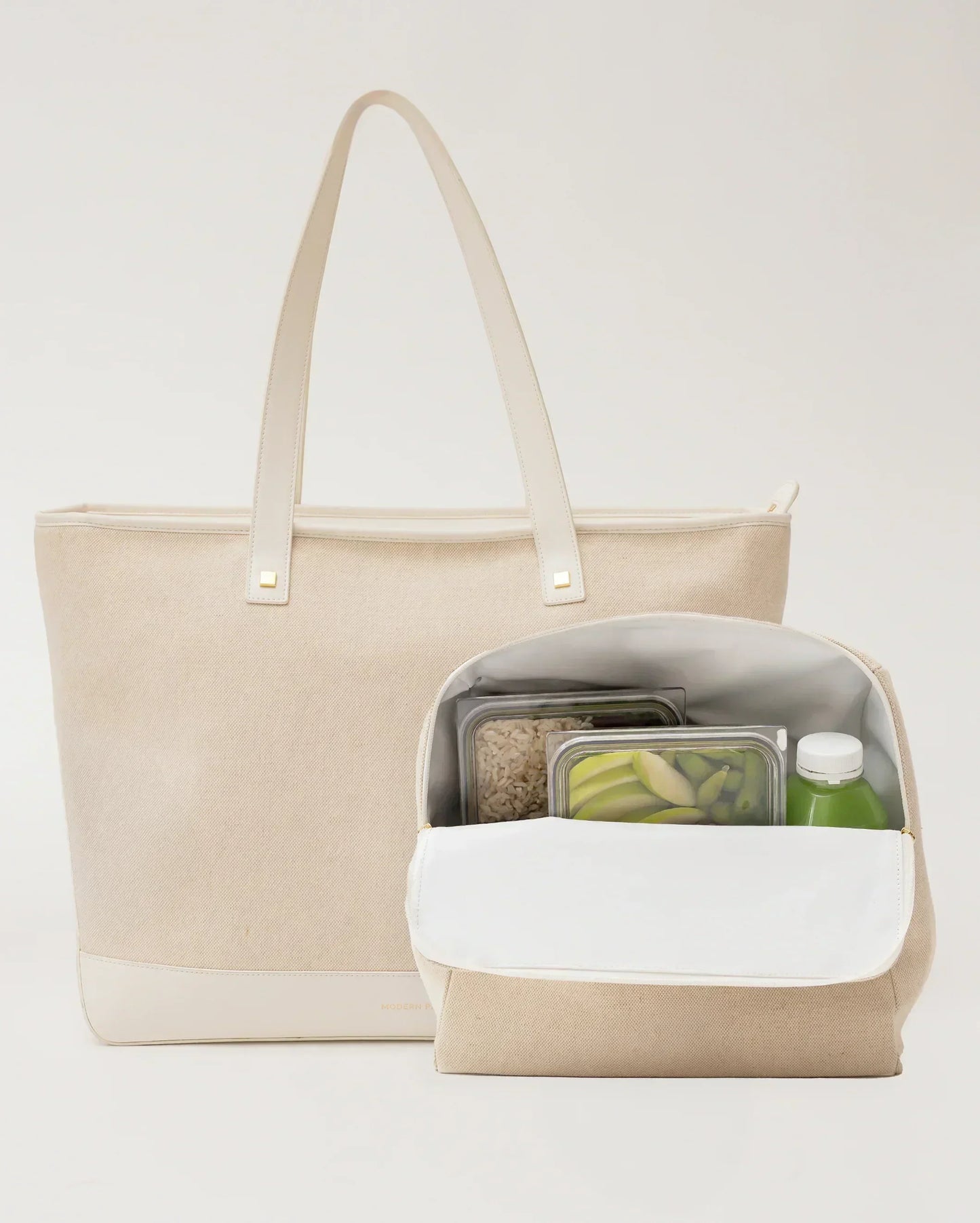 Beige insulated lunch tote with vegan leather handles, holding meal prep containers and a green juice bottle.
