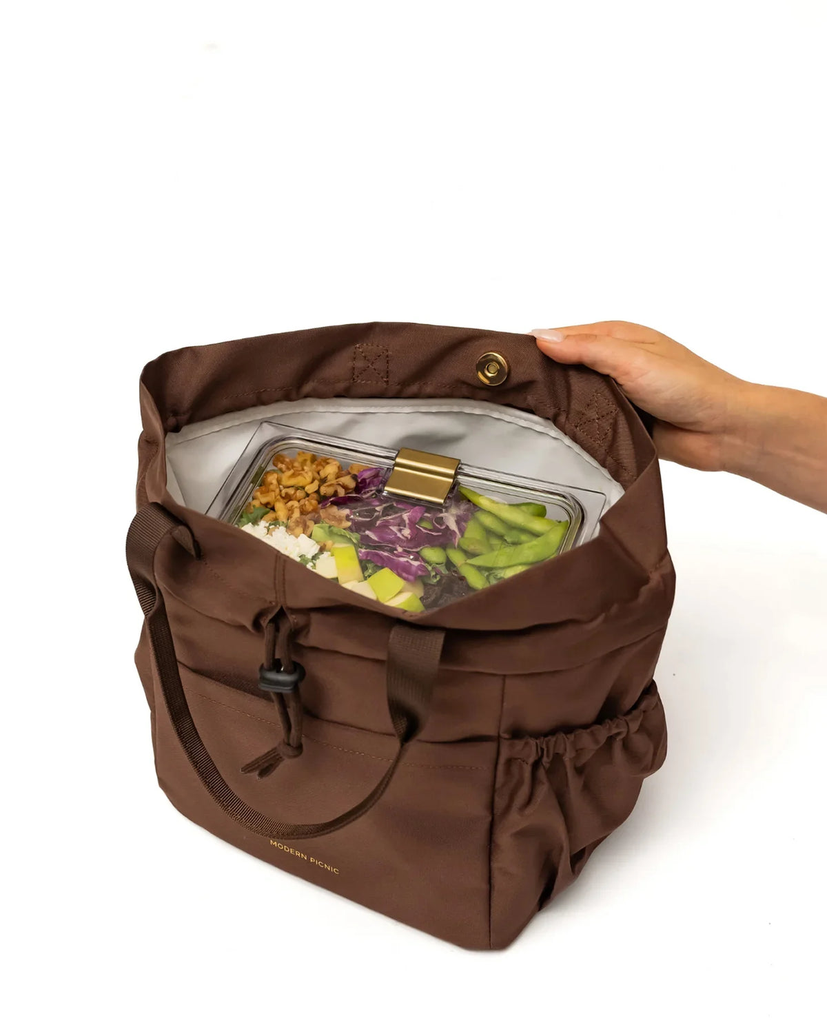 A person opening a brown insulated lunch bag containing a clear container of salad.