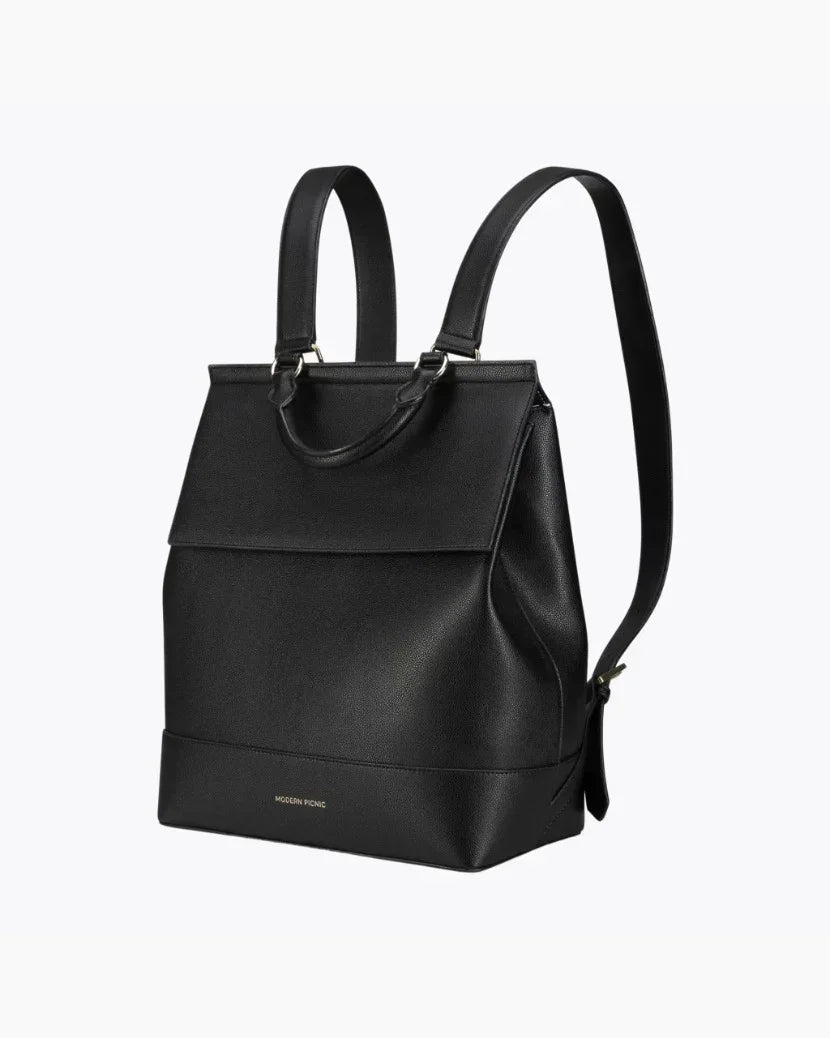 A full-view product photo shot at a side angle of a sleek, structured backpack with top-carry handle and a fold-over flap.