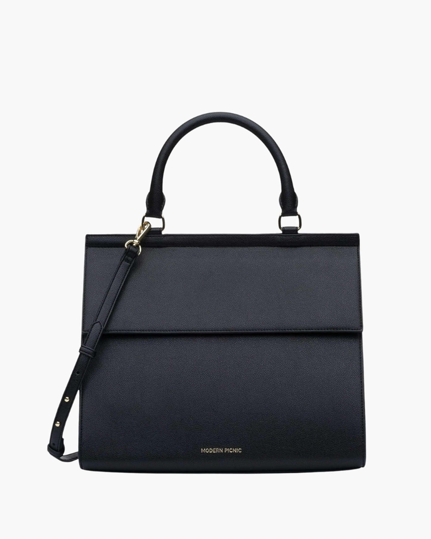 A structured black purse. It features a curved top handle, a fold-over flap closure, a thin, adjustable shoulder strap attached to one side with gold-tone hardware, and the MODERN PICNIC logo subtly stamped in gold near the bottom edge.