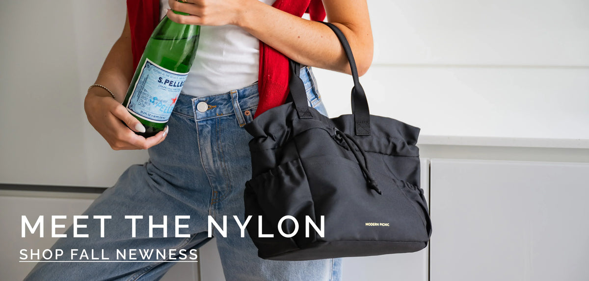 Woman wearing jeans and a red cardigan holding a S.Pellegrino bottle and a black nylon tote bag.