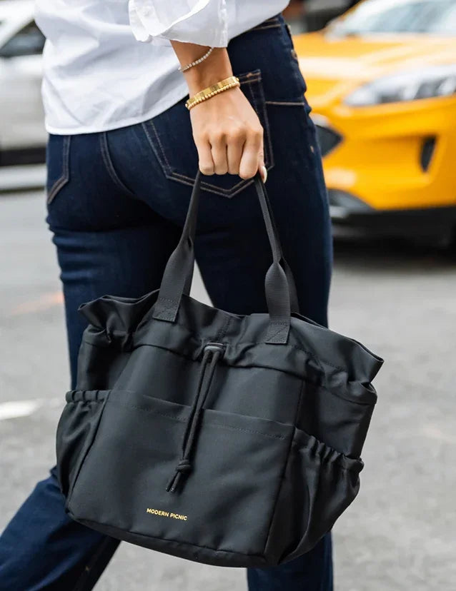 A person carrying a black Modern Picnic insulated tote bag while walking outdoors.