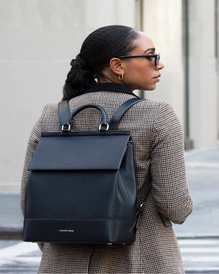 Stylish black vegan leather backpack for work and travel, worn by woman in chic houndstooth coat