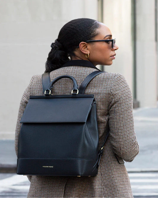 Stylish black vegan leather backpack for work and travel, worn by woman in chic houndstooth coat