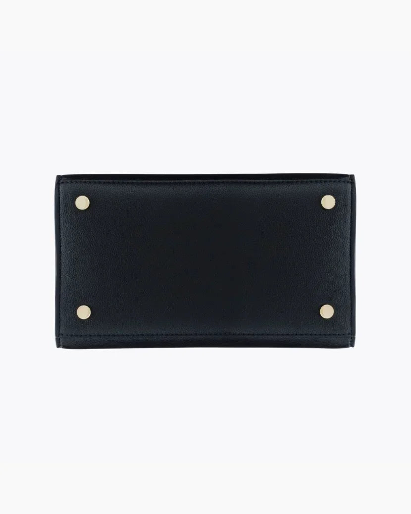 A close-up view of the bottom of the black handbag, showing the flat, structured base made of pebbled vegan leather. The base is protected by four small gold metal feet (studs), one in each corner.