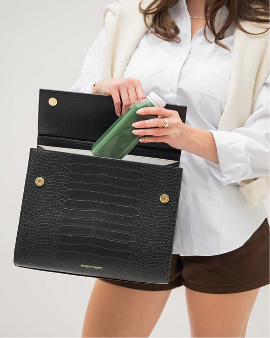 Woman placing a green bottle inside a black croc-embossed insulated lunch bag