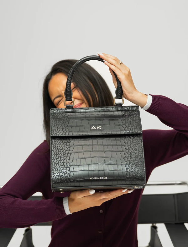 Woman holding a black vegan leather crocodile embossed insulated lunch tote with AK initials.