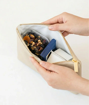Beige insulated lunch bag with nuts, dried fruit, and snacks inside, held by hands