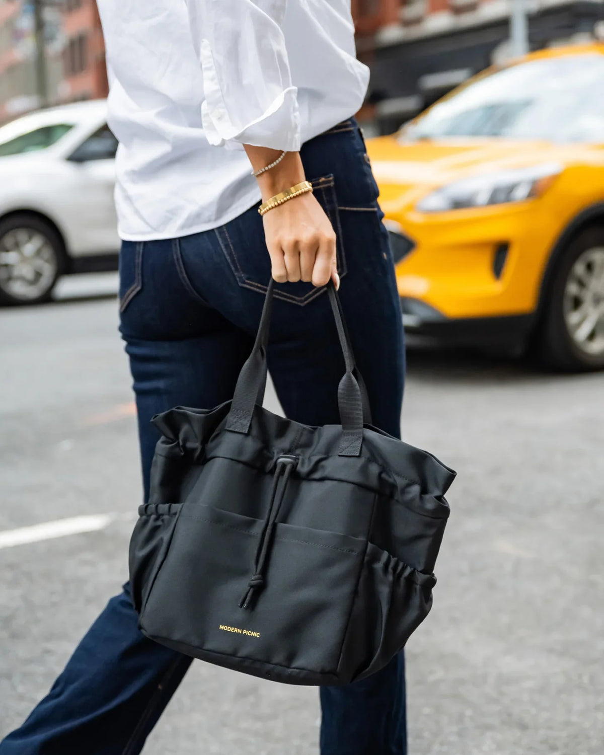 Person carrying a black Modern Picnic insulated lunch tote bag while walking on a city street.