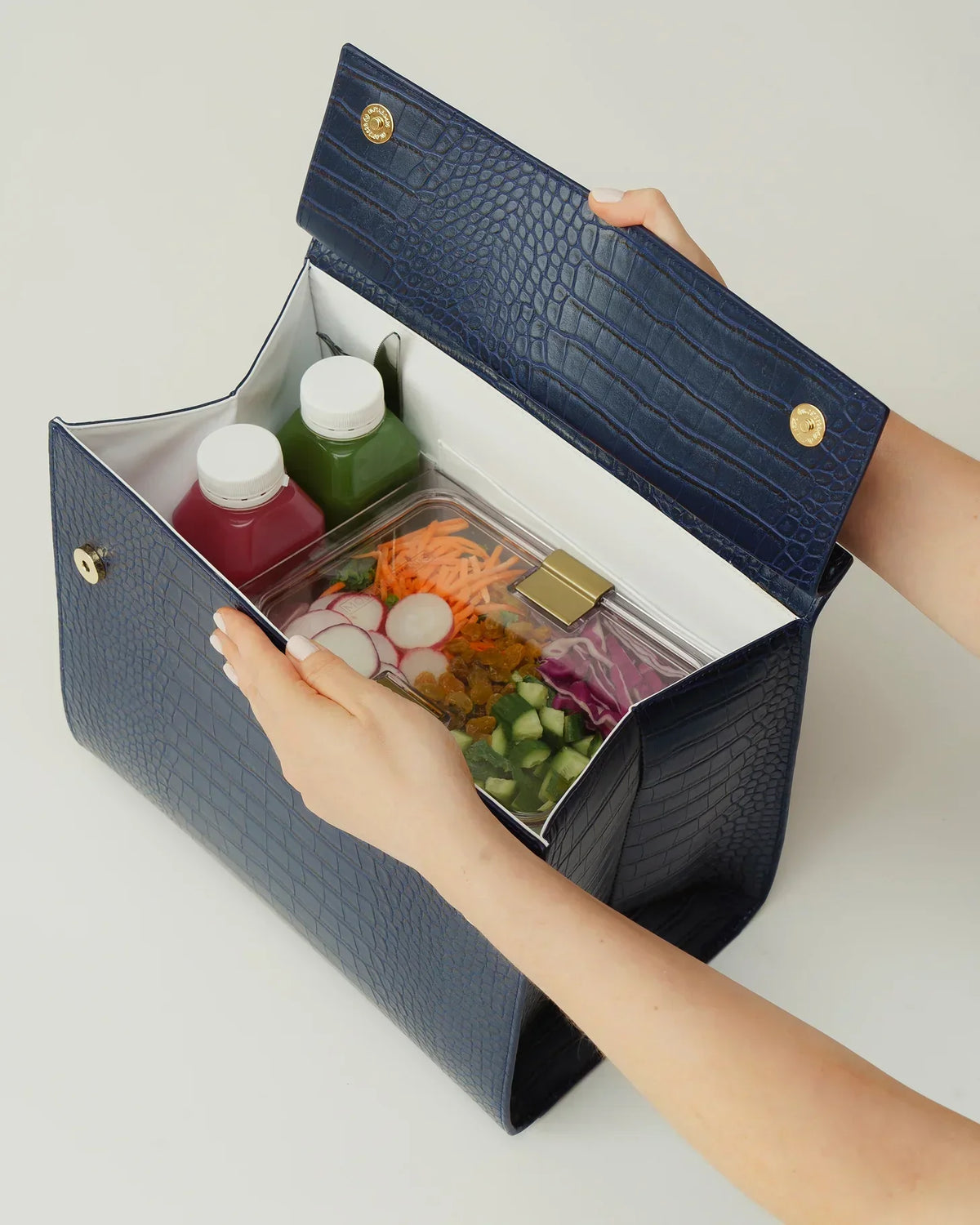 A blue vegan leather insulated lunch bag containing a salad container and two juices.
