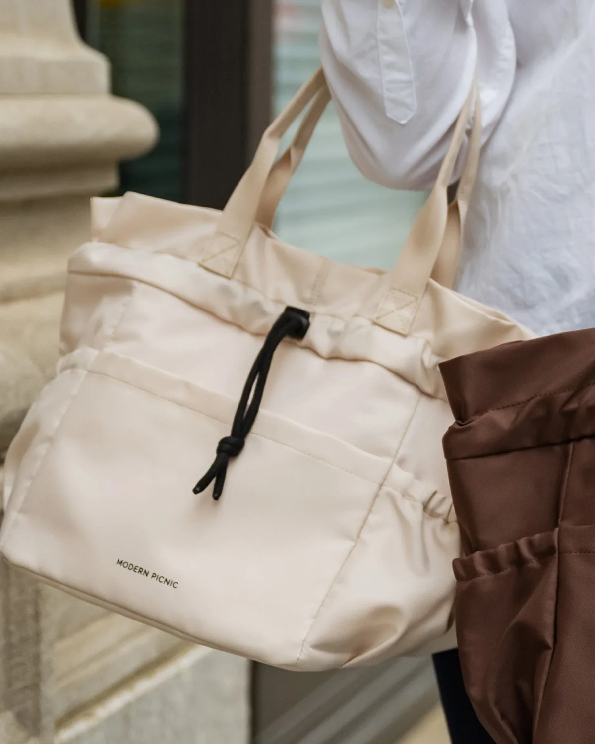 Cream colored insulated vegan leather tote bag being carried by a person.