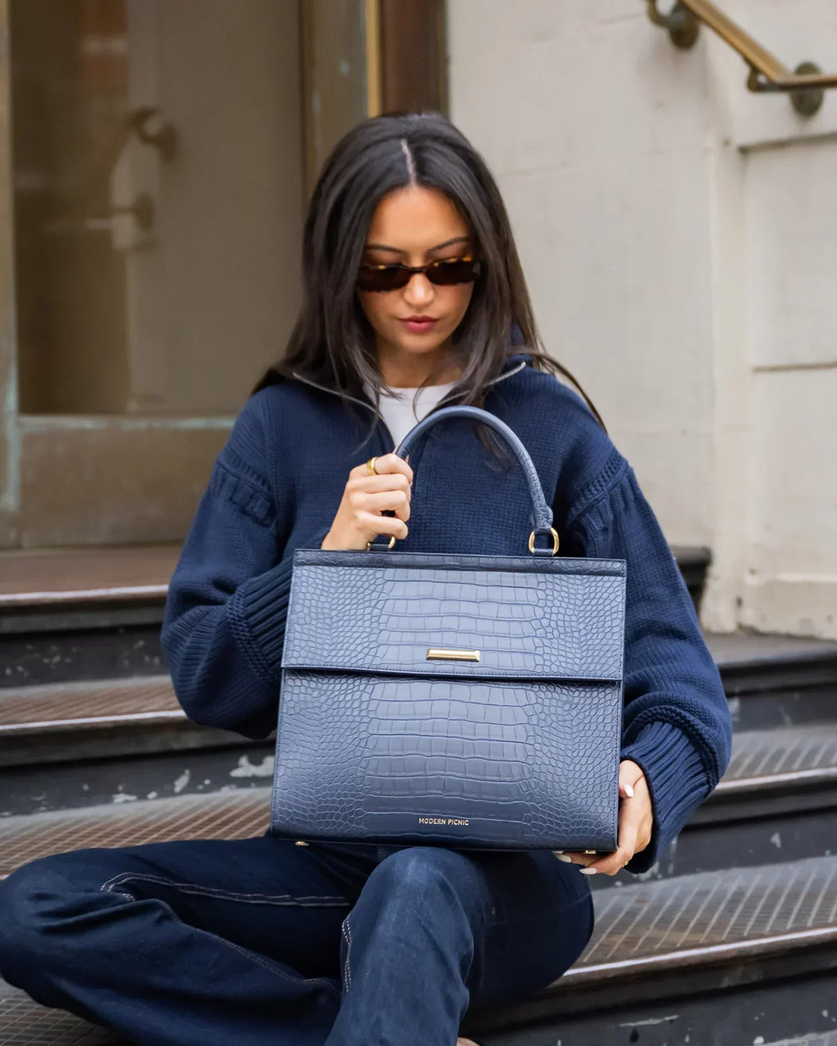 Woman in a navy sweater holding a navy blue croc-embossed vegan leather handbag.