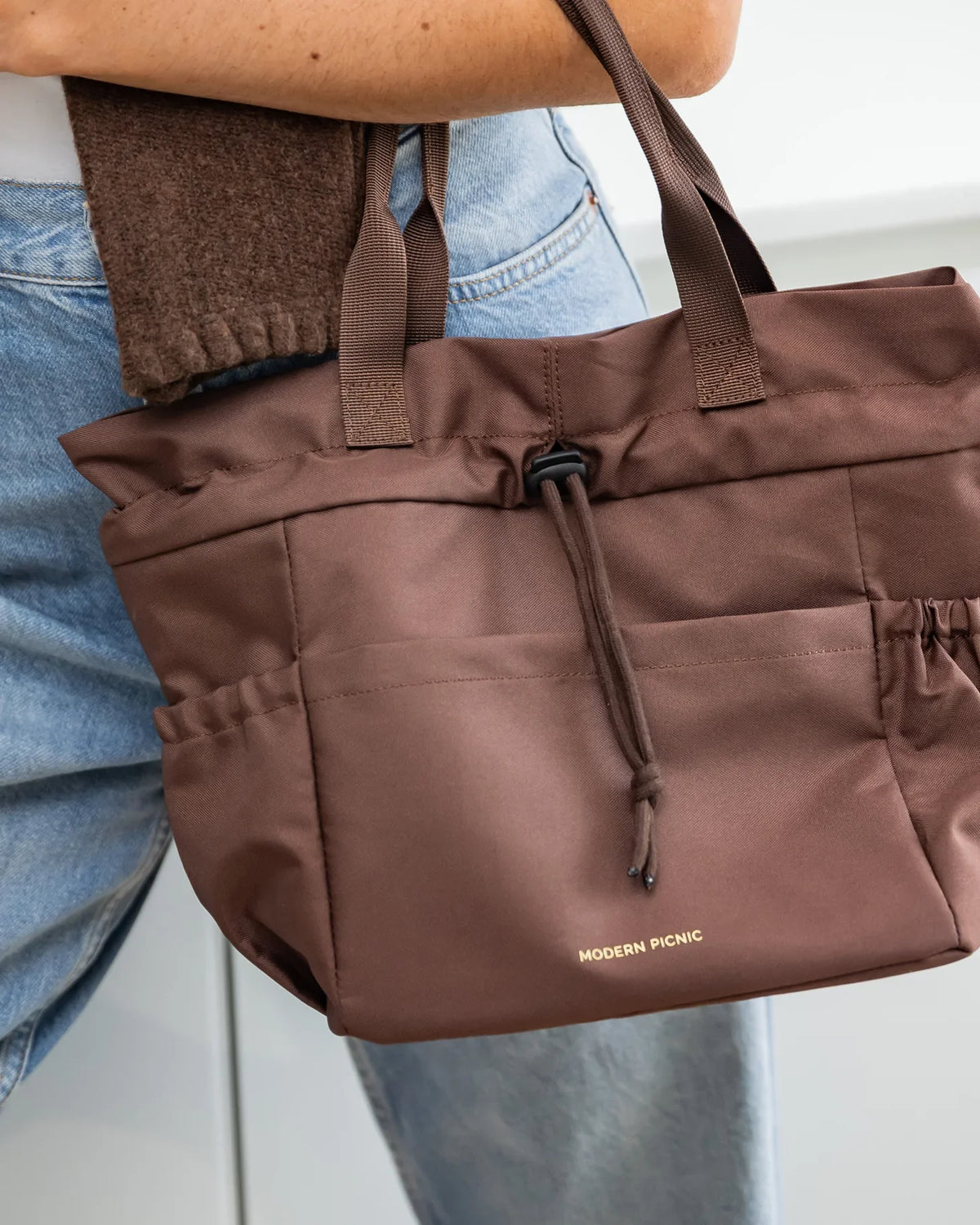 Brown insulated vegan leather tote bag with drawstring closure and side pockets.