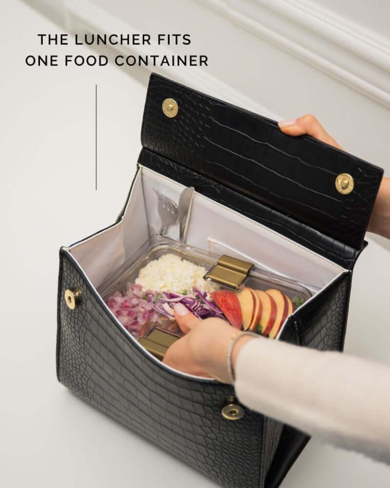 Black textured lunch bag with insulated interior holding a food container with salad and fruit