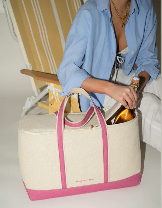 Chic insulated tote bag with pink trim, used for carrying a bottle, beside a striped lounge chair.
