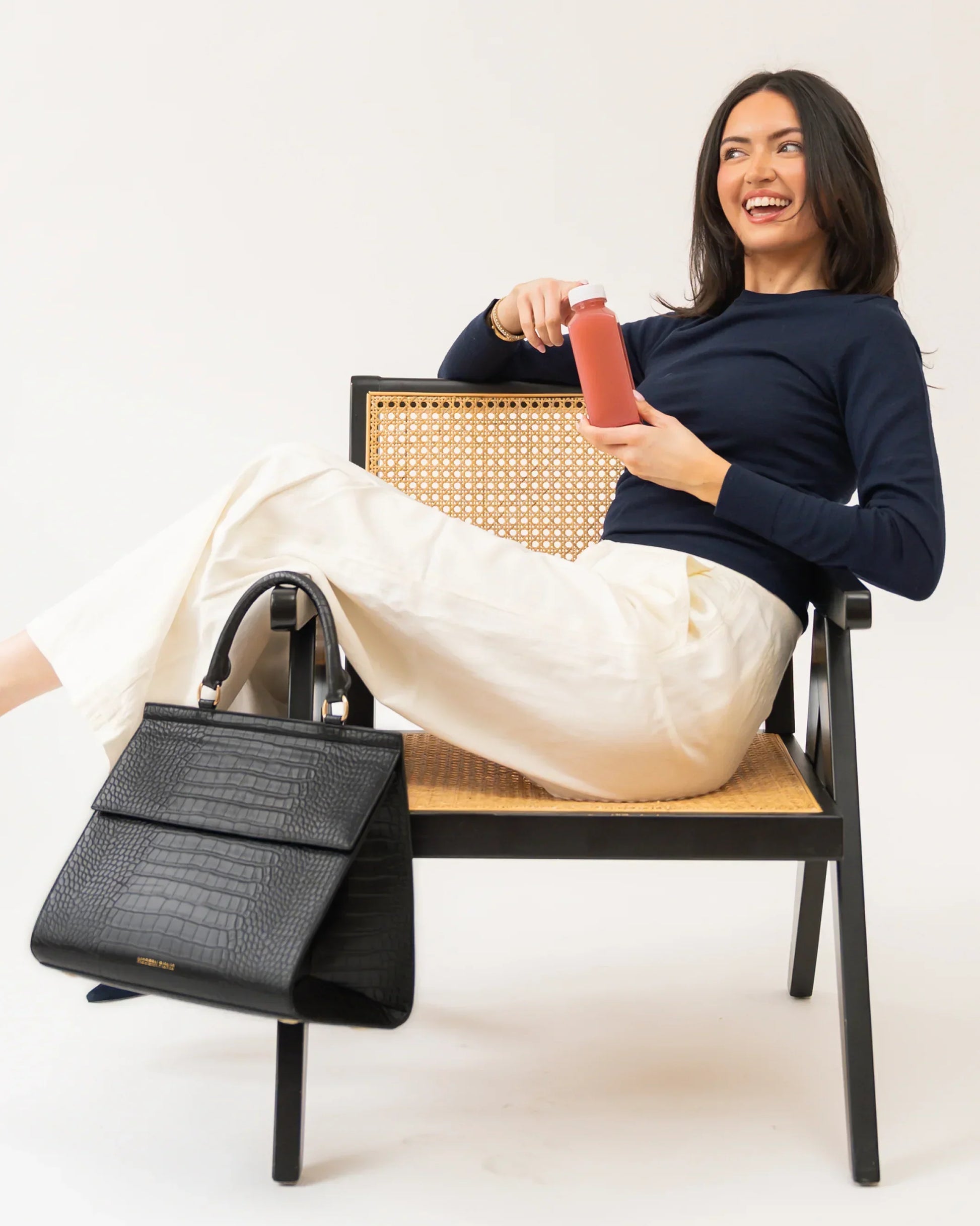 Stylish woman with vegan leather tote, sipping juice, seated on cane chair, chic lunch bag for work or travel