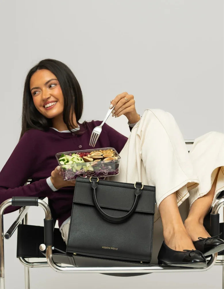Woman in purple sweater eating a salad with a black Modern Picnic insulated lunch bag.