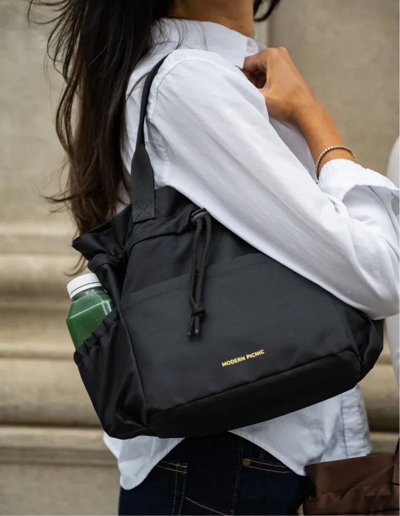 Woman carrying a black Modern Picnic insulated tote bag with a side bottle pocket.