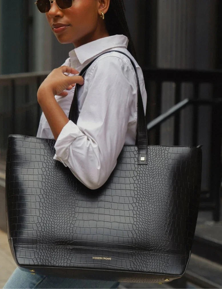Woman in a white button-down shirt carrying a black croc-embossed vegan leather tote bag.