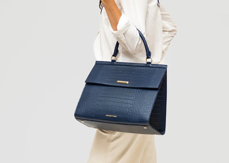 Woman holding a navy blue vegan leather croc-embossed insulated lunch bag.