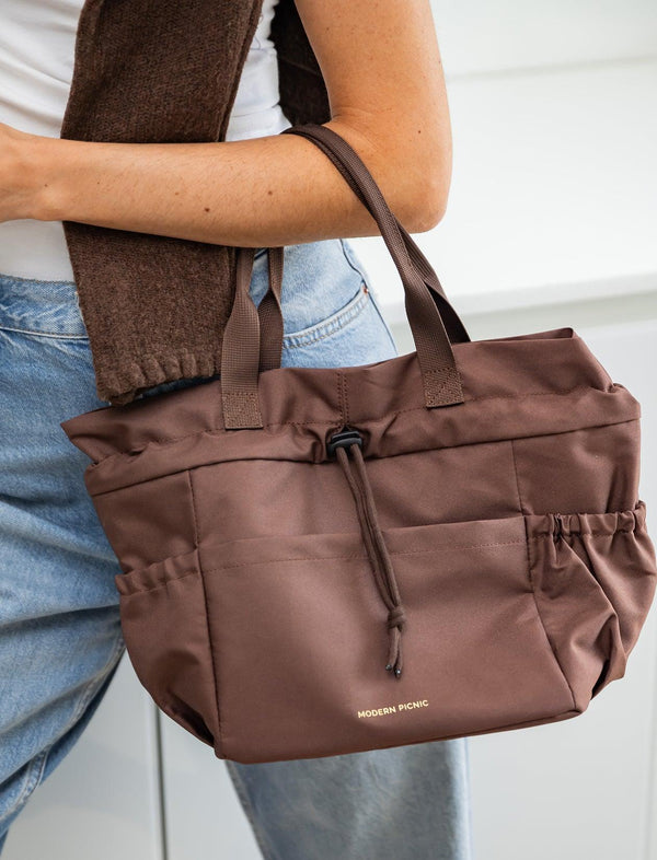 A person carrying a brown Modern Picnic insulated tote bag over their shoulder.